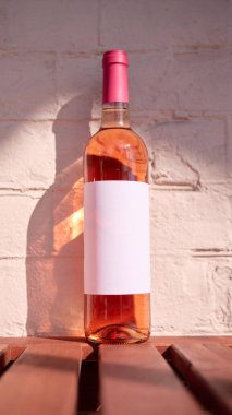 Ahşap masanın üzerinde boş etiketli gül şarabı şişesi, reklam için maket, mesaj. Paketleme tasarımı, markalaşma, menü görselleri, reklam kampanyaları ve yaşam tarzı içeriği kavramı.