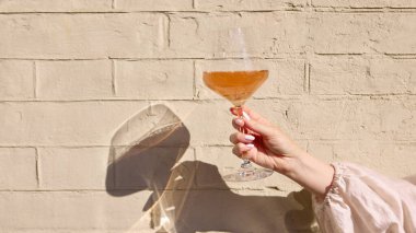 Elinde güneş ışığı ve duvarında yumuşak gölgesi olan gül şarabı kadehi. Etkinlik tanıtımı, bar markalaşması, yaşam tarzı içeriği, alkol turizmi, sosyal medya ve eğlence kavramı.