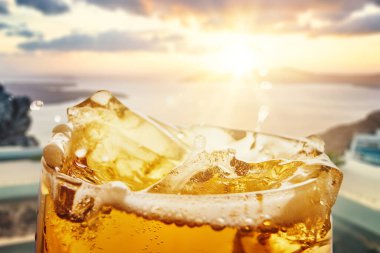Altın günbatımı arkaplanlı bardağa bira sıçratmak. Tazelik, içecek reklamı, markalaşma, yaşam tarzı, yaz tatili, neşe, kutlama ve susuzluk kavramı..