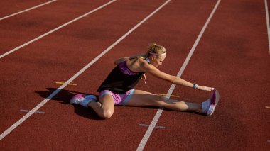 Sporcu, sakin bir odak ve disiplinle oynanan bir yarışmadan önce pistte geriliyor. Isınma, esneme, esneklik, vücut hazırlığı, fiziksel sağlık ve atletik performans kavramı.