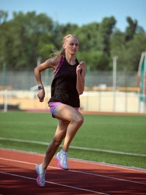 Genç bir kadın yemyeşil bir manzarayla çevrili bir pistte koşuyor. Güç kavramı, sprint hareketi, dinamik enerji, güçlü bitiş, atletik kararlılık.