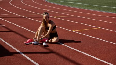 Pistte oturan bayan koşucu engelli antrenmanından önce odaklanarak viraja giriyor. Atletizm sporu ve eğitiminde adım adım hazırlık, disiplin ve büyüme kavramı.