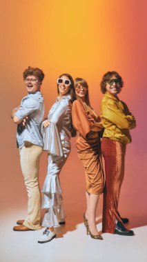 Retro grubu, turuncu arka planda disko modasında sırt sırta poz veriyor. Klasik tarz kavramı, popüler kültür nostaljisi, birlik, arkadaşlık ve cesur yaşam tarzı enerjisi..