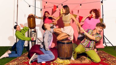 Genç bir kadın fıçıda oturmuş arkadaşlarıyla gülerek erkeklerin ağzına içki dolduruyor. Spontane eğlence, içecek kültürü, genel z arkadaşlık ve şenlikli parti havası kavramı..