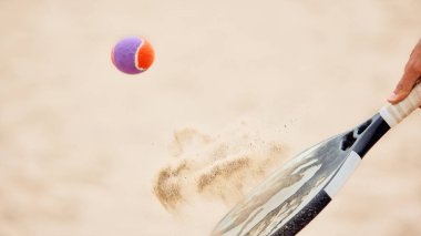 Padel raketi kum kumsalında uçan kum taneleriyle topa vuruyor. Hareket kavramı, spor dinamiği, fitness yaşam tarzı, enerji, sosyal medya ve dijital pazarlama görselleri.