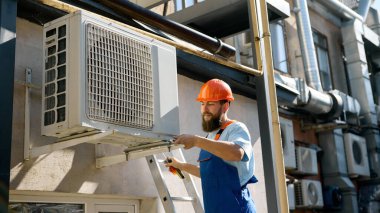 Technician installing air conditioning unit outdoors. Concept of engineering services, HVAC maintenance, and workplace safety with focus and confidence.