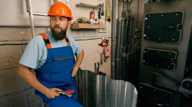 Technician resting after maintenance work near heating system. Concept of occupational safety, engineering labor, and moment of recovery with calm and satisfaction.