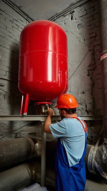 Engineer inspecting large red pressure tank in industrial room. Concept of engineering services, occupational safety, technical precision, responsibility, and reliability.