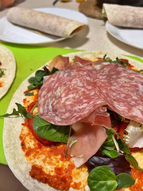 Tortilla, salam, çiğ Parma jambonu, roka, ayvar biberi sosu, tortillaların üzerine ürün koymak, tortilla sarmak