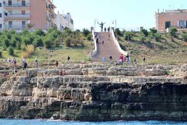 Kumsalda köprü, Polignano körfezi güney İtalya 'da basit beyaz binalar, kıyıda düz kayalar, kayaların arasında sahil, platoda merdivenler.