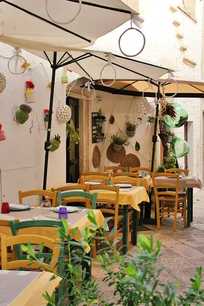 tables in front of the restaurant, umbrellas over the tables, decorations around the restaurant, tablecloths on the tables, Mediterranean atmosphere