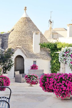 İtalyan kasabasında dar bir sokak, beyaz evler, beyaz şehir, beyaz taş binalar, Alberobello kasabası, İtalya, evin yanına yerleştirilmiş bitkiler, pembe petunyalar, trulli evler.
