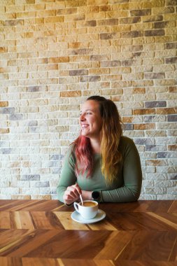 Bir kafede bir fincan kahveyle oturan, gülümseyen bir kadın.