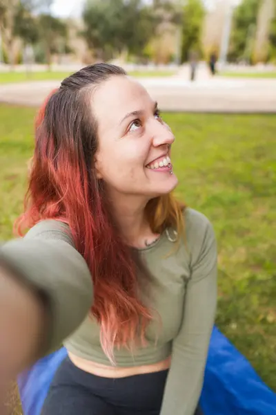 Parkta selfie çekerken gülümseyen ve başka tarafa bakan bir kadın..