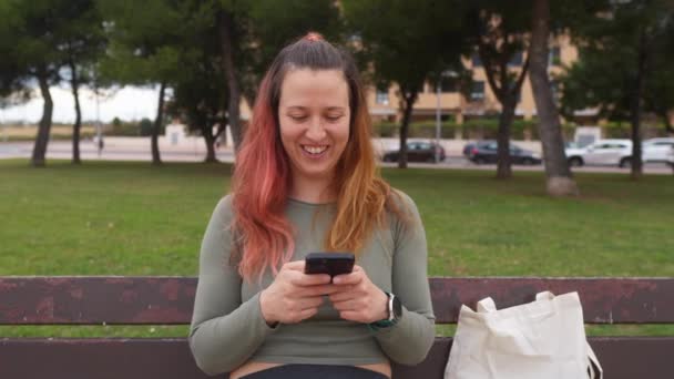 Una Mujer Sonriente Usando Teléfono Inteligente Mientras Está Sentada Banco — Vídeos de Stock