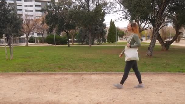 Mujer Caminando Con Una Bolsa Mano Través Parque Mirando Hacia — Vídeo de stock
