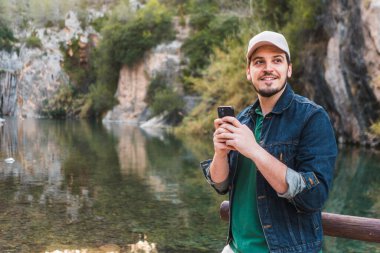 Nehir kenarında elinde telefon tutan dalgın bir adam..
