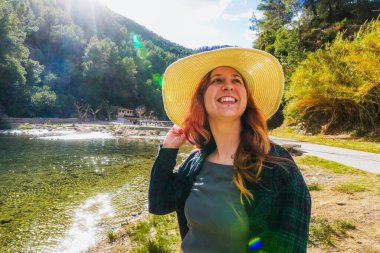 Güneş şapkalı kadın, nehrin kenarında gün ışığının tadını çıkarıyor..