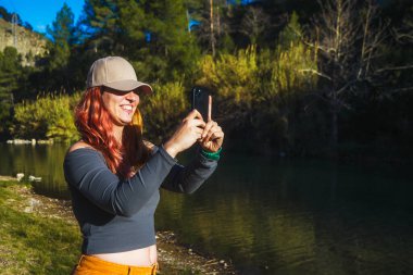 Açık havada akıllı telefonunu kullanan şapkalı, gülümseyen kadın..