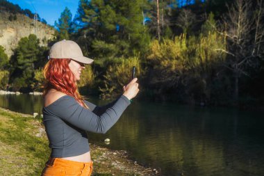 Kızıl saçlı kadın nehir kenarında selfie çekiyor..
