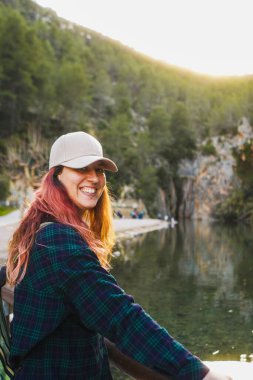 Gün batımında dingin bir nehrin kenarında şapkalı, gülümseyen bir kadın..