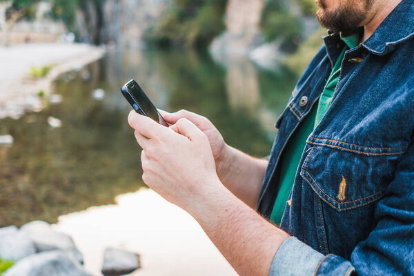 Мужчина пишет смс по телефону у реки.
