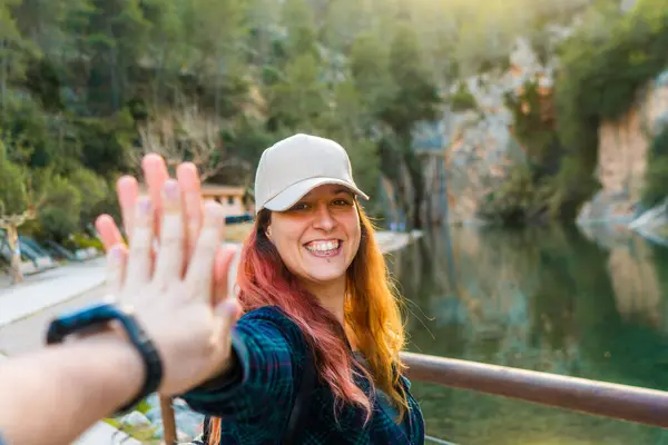 Woman in a cap giving a high-five by the river.