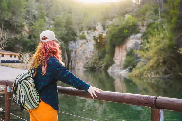 Köprüde nehire bakan kızıl saçlı kadın.