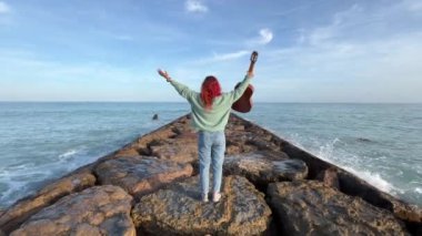 Akdeniz 'de gitardan esinlenilmek üzere nefes alan ve kollarını uzatan bir kadının arka planı. Arka planda deniz var.