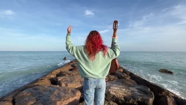 女人呼吸着 伸出她的胳膊 在地中海防波堤上弹奏吉它 背景是大海 — 图库视频影像