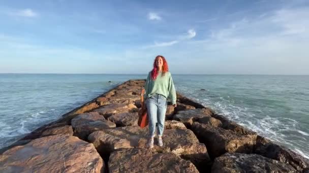 地中海のブレイクウォーターに沿ってギターを歩く女性 フロントビュー — ストック動画