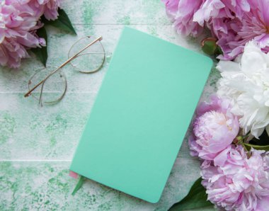 Düz kağıt defter, gözlükler, yeşil ahşap arka planda şakayık çiçekleri.