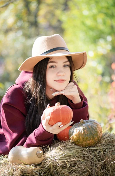 白人の少女は秋の公園に座っている 彼女はオレンジのカボチャを手に持っている — ストック写真