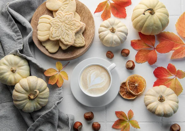 Cozy autumn composition. Hot coffee with cookies in a white cup  surrounded by autumn leaves and pumpkins on a white wooden background.