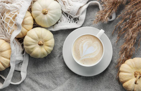 White pumpkins, coffee and pampas grass on a grey textile background. Autumn home decor.