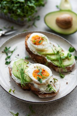 Bread toast, boiled eggs, avocado slice, microgreens on a plate, breakfast time