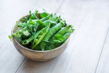 Bowl with young fresh juicy pods of green peas on a wooden background. Healthy organic food. 