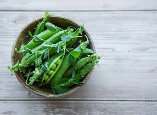 stock image Bowl with young fresh juicy pods of green peas on a wooden background. Healthy organic food. 