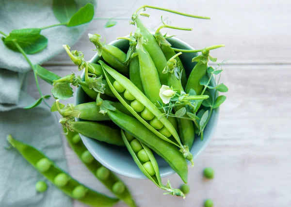 stock image Bowl with young fresh juicy pods of green peas on a wooden background. Healthy organic food. 