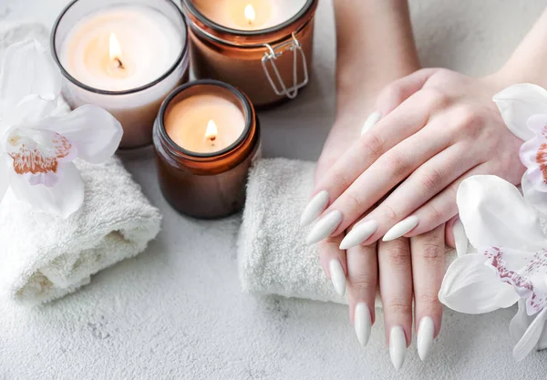 漂亮的手一个年轻的女人与白色指甲修指甲 在美甲沙龙的毛巾 蜡烛和白兰花上的女性手 — 图库照片