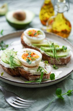 Bread toast, boiled eggs, avocado slice, microgreens on a plate, breakfast time