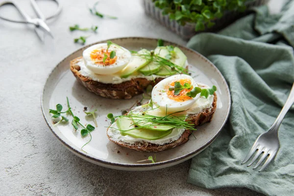 stock image Bread toast, boiled eggs, avocado slice, microgreens on a plate, breakfast time