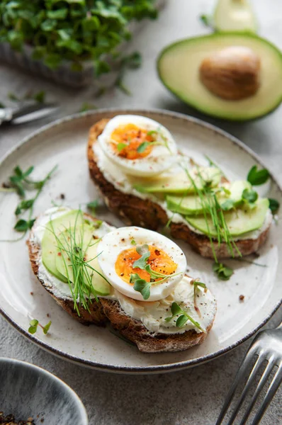 stock image Bread toast, boiled eggs, avocado slice, microgreens on a plate, breakfast time