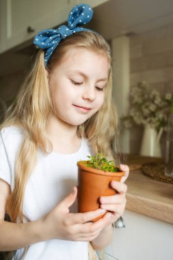 Küçük kız mutfağında oturuyor ve elinde fidelerle bekliyor.