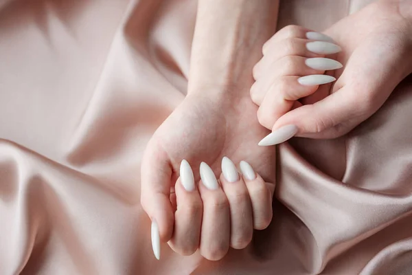 Красивые Руки Молодой Женщины Белым Маникюром Ногтях Бежевый Шелковый Фон — стоковое фото