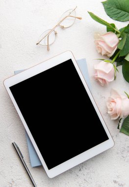 Beton arka planda gül buketi ve tablet. Üst görünüm.