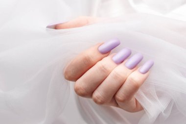 Yumuşak mor manikürlü bir kızın elleri. İpek ve tülden oluşan beyaz bir arka plan. Güzellik ve özen kavramı.
