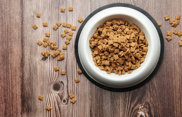 A bowl of dog food on a wooden floor. Dry food in granules.