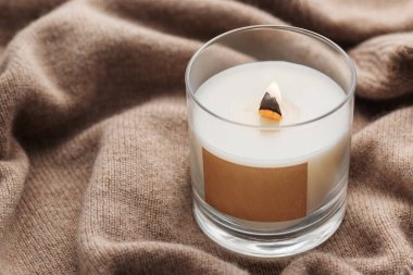 A candle burns on the background of a knitted sweater. The concept of cozy winter or autumn.