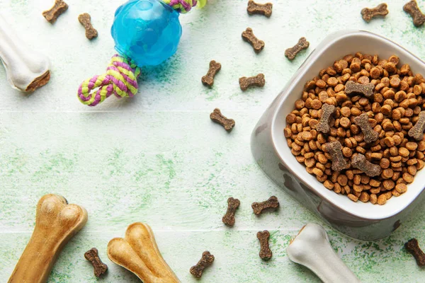 A bowl with dog food, dog treats and toys on a wooden floor. Concept of healthy food for dogs.